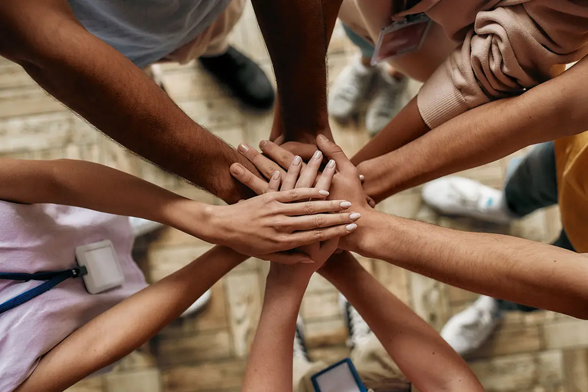 Group of men and women with hands on top of each other.